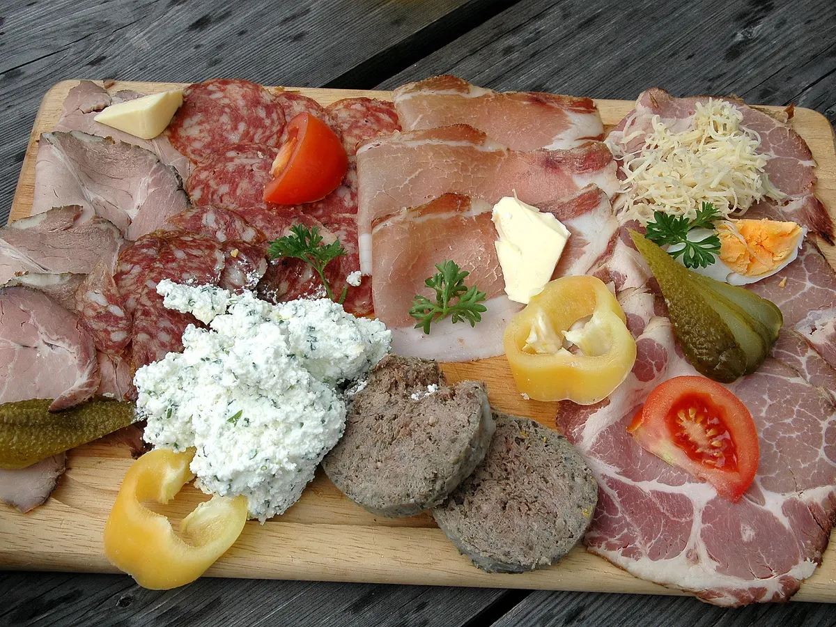 Holzbrett mit Schinken, Speck, Salami, Frischkäse, Paprika und Gewürzgurken