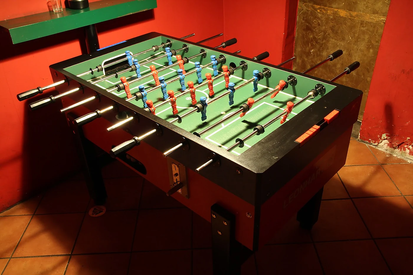 Kickertisch mit blauen und roten Figuren in einem Raum mit roten Wänden und Terrakottafliesen