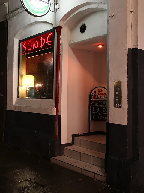 Eingang der Bar SÜNDE bei Nacht mit rotem Neonschild über dem Fenster und ein paar Stufen zur Tür