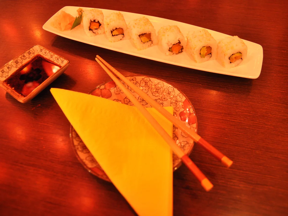 Maki-Rollen mit Sojasauce und Stäbchen auf rotem Tisch