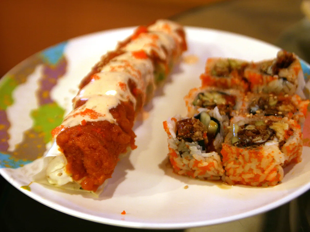 Zwei Sushi-Rollen mit Chilisauce und Sesam auf weißem Teller
