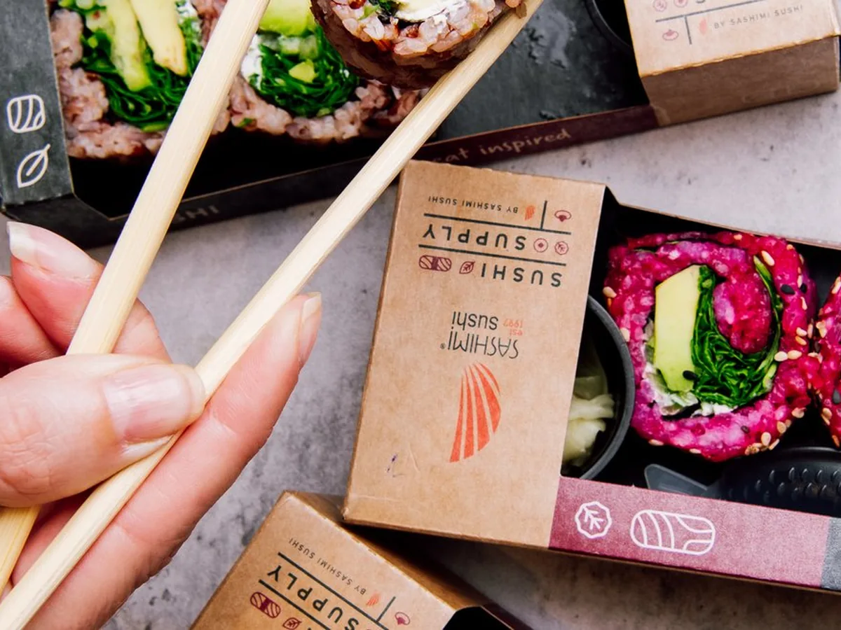Hand mit Essstäbchen über geöffneten Sushi-Boxen