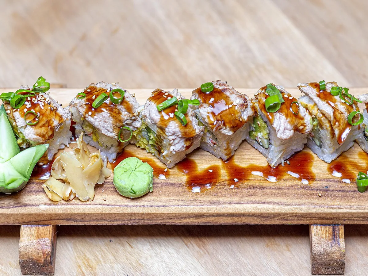 Reihe Maki-Rollen mit Sauce und Sesam auf einem Holzbrett