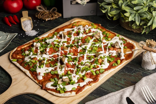 Flammkuchen mit Tomatensauce, Champignons, Frühlingszwiebeln und Crème fraîche auf einem Holzbrett