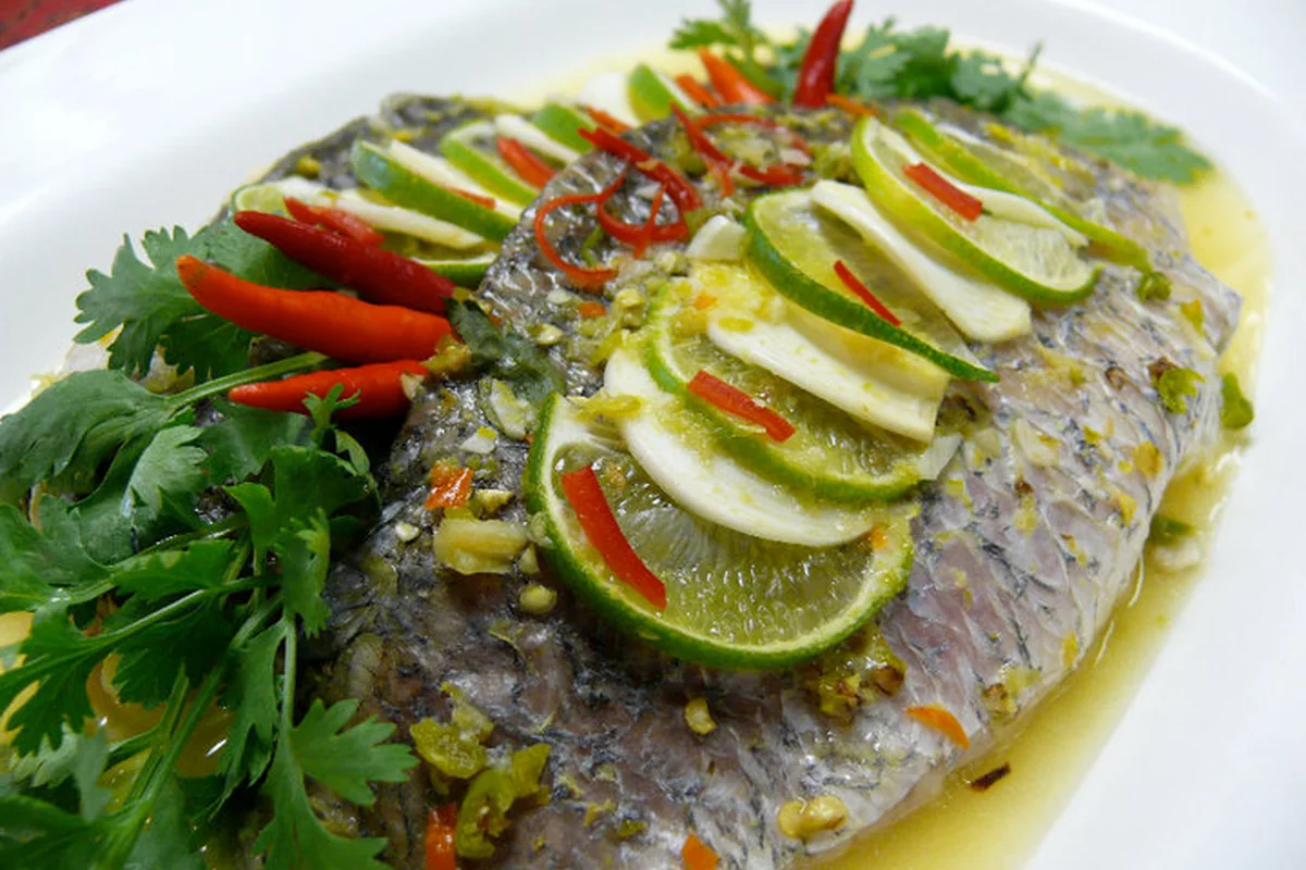 Gedämpfter ganzer Fisch mit Limettenscheiben, roten Chilistreifen und Koriander