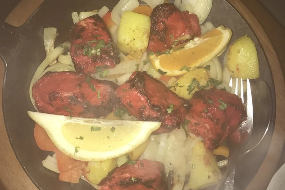 Tandoori-Hähnchenstücke mit Zwiebeln, Kartoffeln und Zitronenspalten in einer Metallpfanne