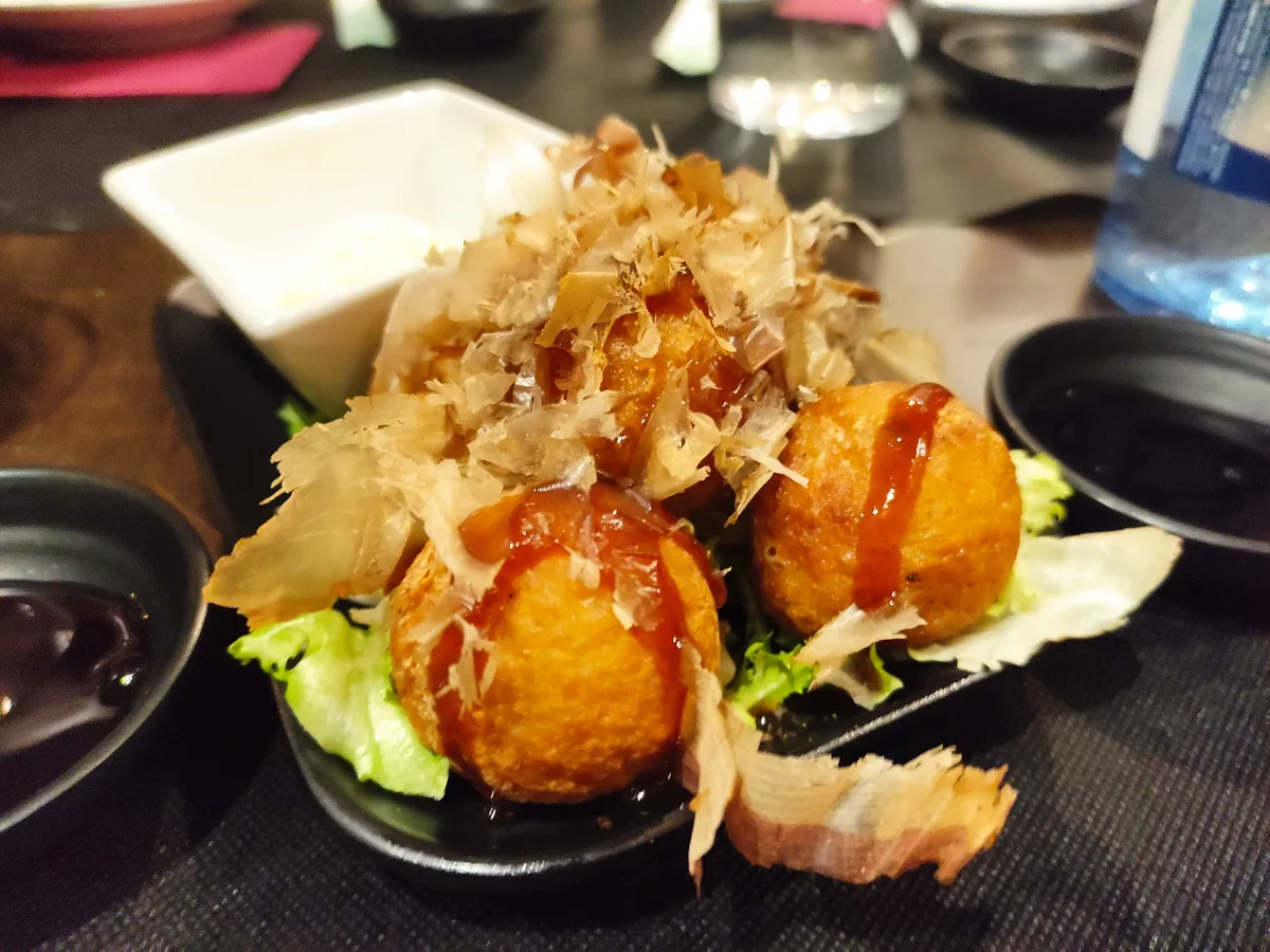 Takoyaki-Bällchen mit Sauce und Bonitoflocken auf einem schwarzen Teller