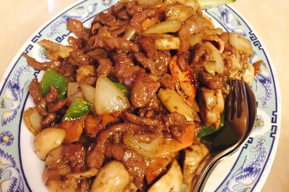 Wok-Gericht mit Rindfleisch, Garnelen und Paprika auf einem blau-weißen Porzellanteller