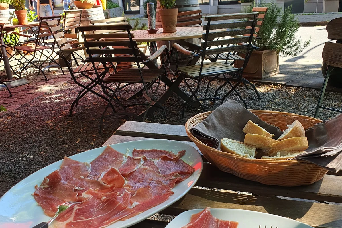 Teller mit hauchdünn geschnittenem Serranoschinken, daneben ein Korb mit Weißbrot auf der Terrasse