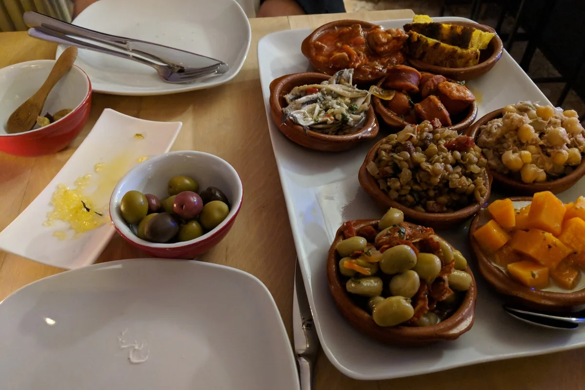 Große Platte mit Tonschälchen voller Tapas, dazu eine Schale gemischter Oliven