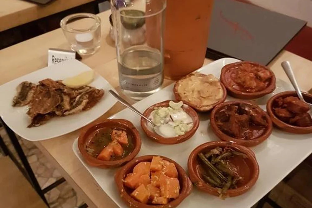 Große Platte mit vielen Tonschälchen voller Tapas, dazu eine Schale Oliven