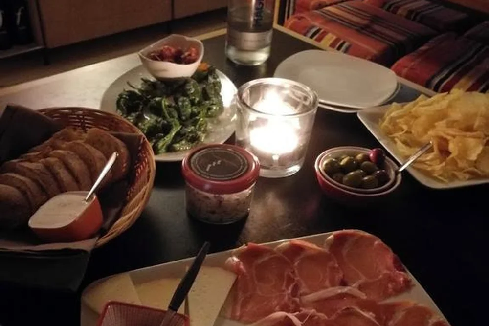 Holzbrett mit Serranoschinken, Käsestücken und einer Schale Marmelade