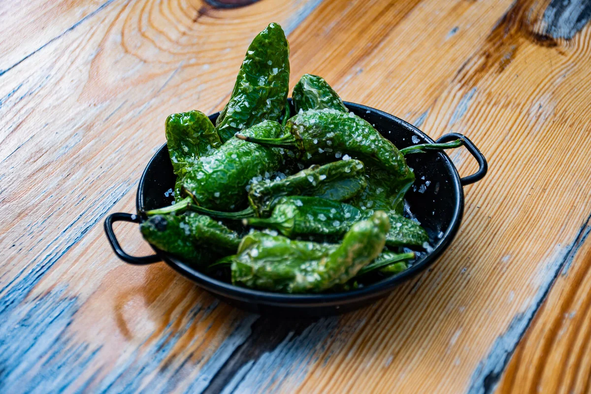 Gebratene Pimientos de Padrón mit grobem Meersalz in einer schwarzen Tapas-Pfanne
