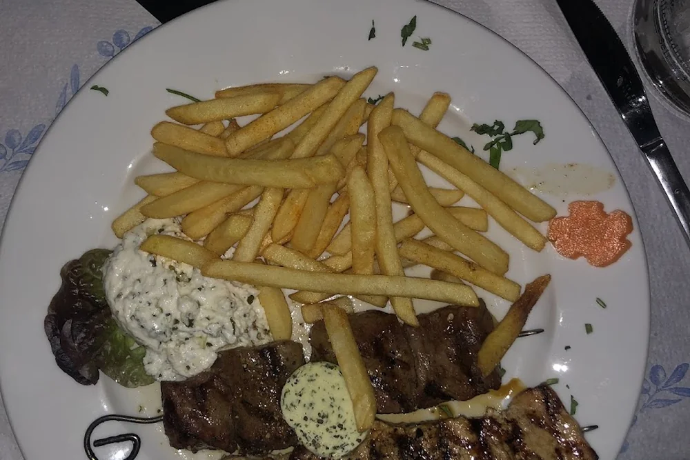 Grillspieß und Steak mit Kräuterbutter, Pommes frites und Tzatziki auf einem Teller mit blauem Rand