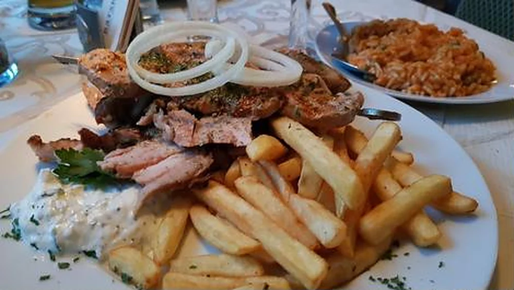 Grillteller mit Steak, Gyros, Zwiebelringen und Pommes frites, dahinter Tomatenreis
