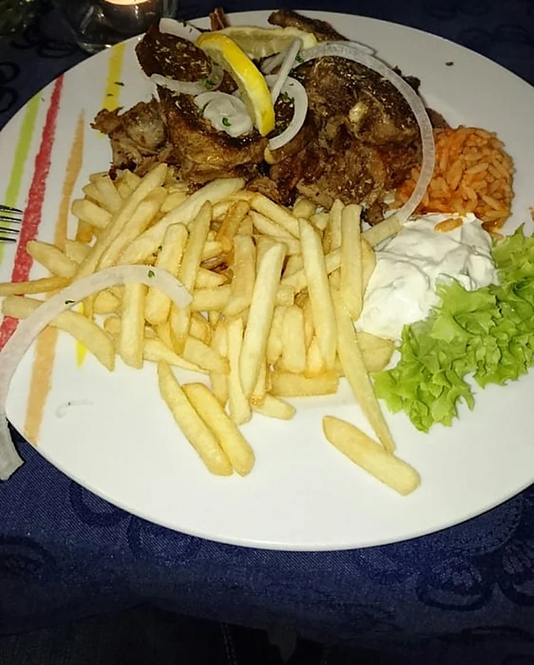 Lammkoteletts mit Zwiebelringen und Zitrone, dazu Pommes frites, Tomatenreis, Tzatziki und Salat