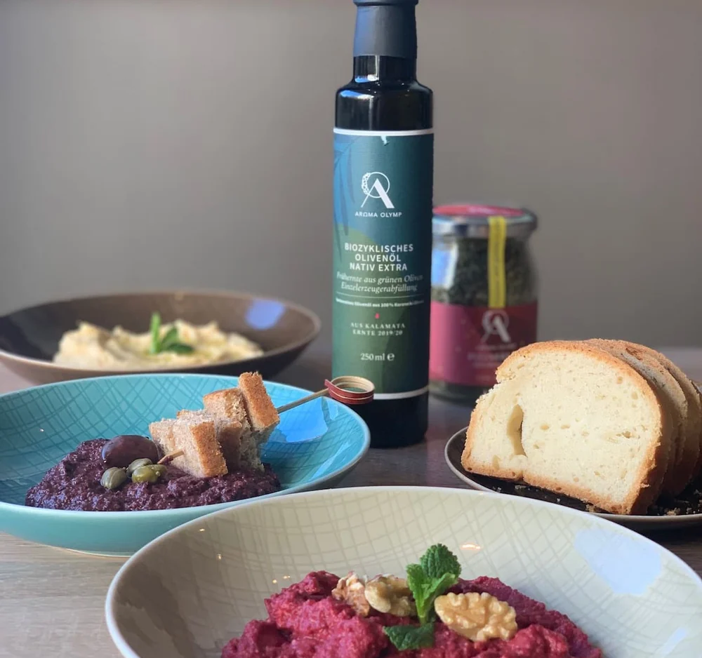Mezze-Schalen mit Rote-Bete-Walnuss-Dip, Melitzanosalata mit Oliven und Brot, dahinter eine Flasche Olivenöl