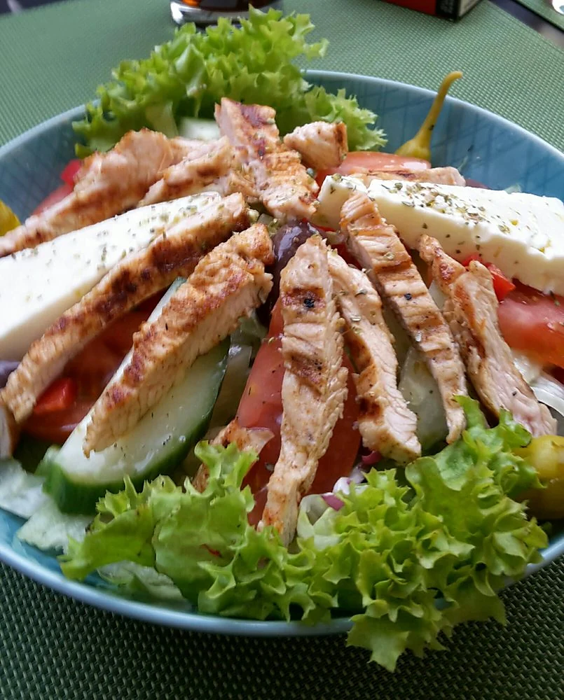 Salat mit gegrillten Putenbruststreifen, Feta, Tomaten, Gurke und Peperoni in einer Schale