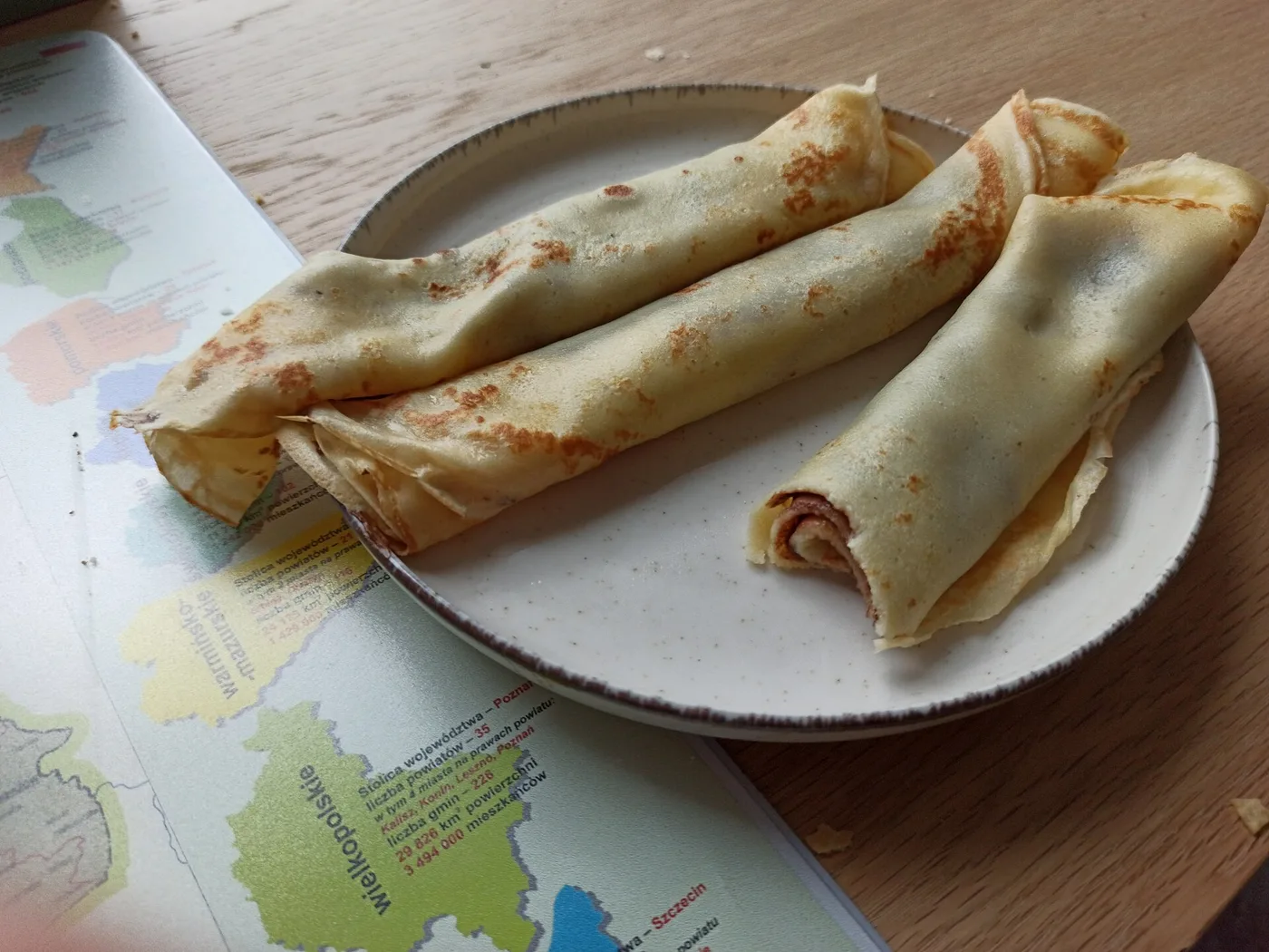 Drei gerollte Pfannkuchen auf einem Teller neben einer Landkarte von Polen