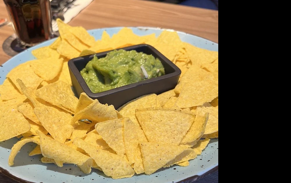 Nachos auf hellblauem Teller mit Guacamole in schwarzer Schale