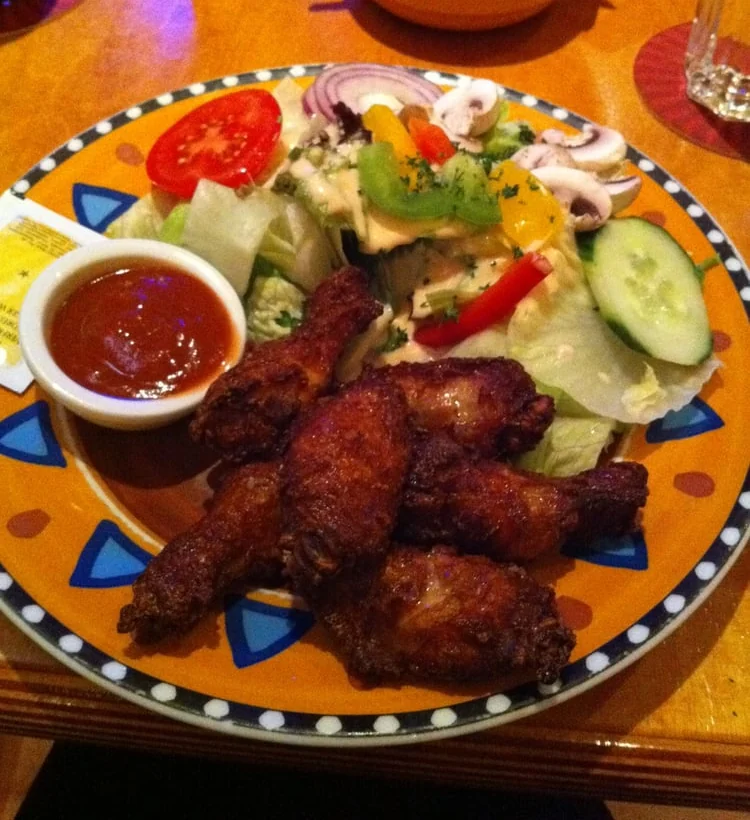 Chicken Wings mit Barbecue-Dip und Salat auf buntem Teller
