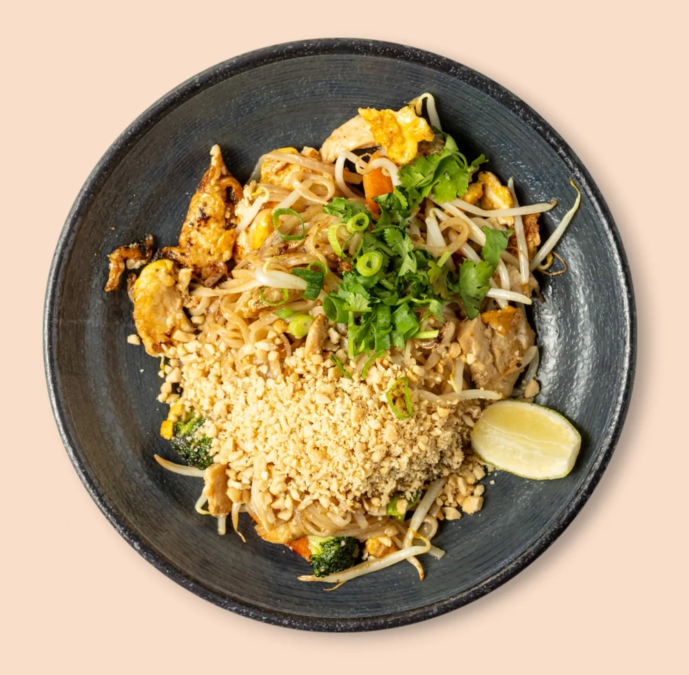 Pad Thai mit gebratenen Reisnudeln, Ei, Sprossen, Erdnüssen, Koriander und Limette auf schwarzem Teller