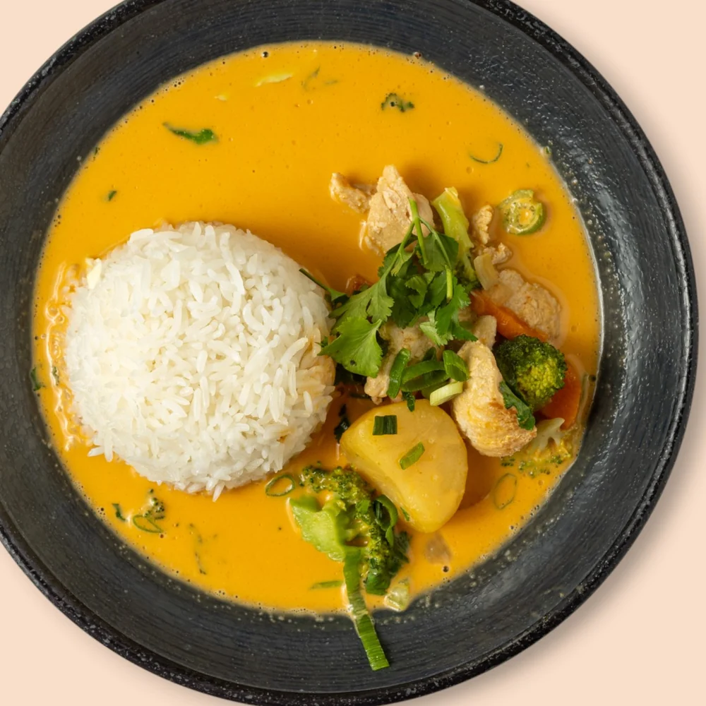 Rotes Thai-Curry mit Kokosmilch, Gemüse und Huhn, dazu Jasminreis auf schwarzem Teller