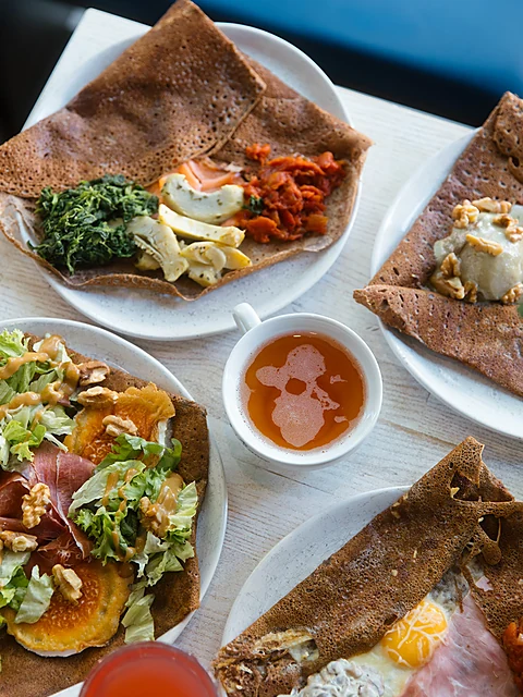 Vier Galettes von oben mit Spinat, Lachs, Ziegenkäse und Walnüssen, Serrano und Salat, in der Mitte Cidre in einer Tasse