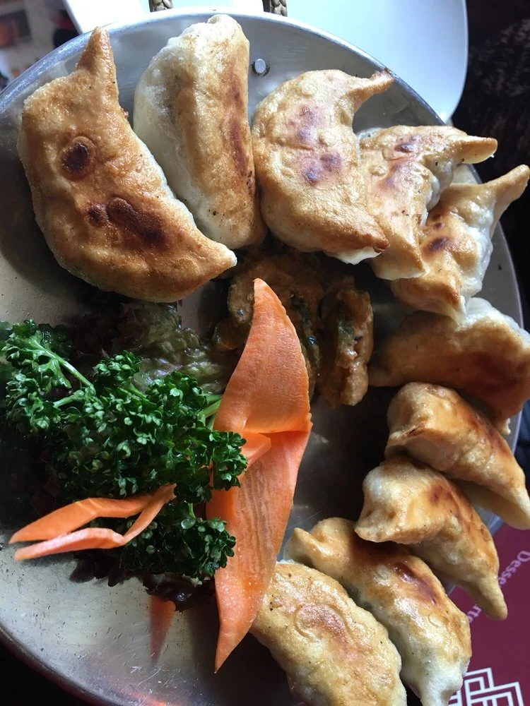 Gebratene Momo, tibetische Teigtaschen, mit Petersilie und Möhrenstreifen auf Metallteller