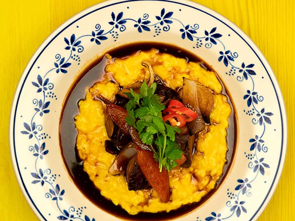 Lomo Saltado mit Wok-Rindfleisch, Zwiebeln, Chili und Koriander auf cremiger Polenta, blau-weißer Teller