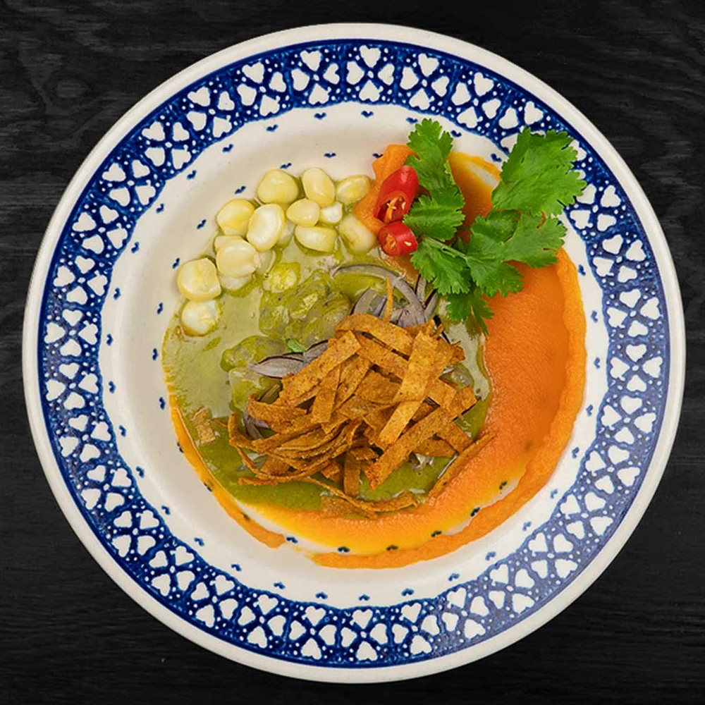 Ceviche Verde mit Choclo-Mais, Tortillastreifen, roten Zwiebeln und Koriander auf blau-weißem Teller