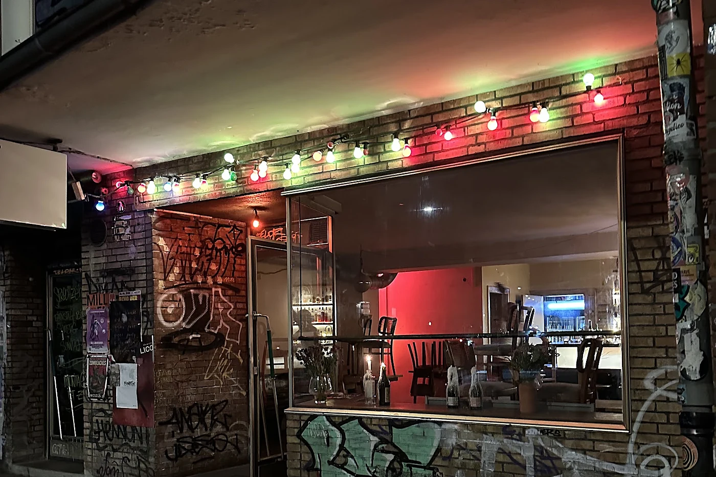 Fassade der Toast Bar bei Nacht mit bunter Lichterkette, Graffiti und großem Fenster