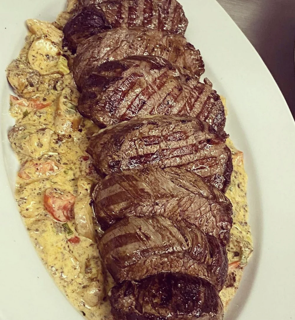 In Scheiben geschnittenes Rindersteak auf cremiger Pasta mit Tomaten auf ovaler Platte