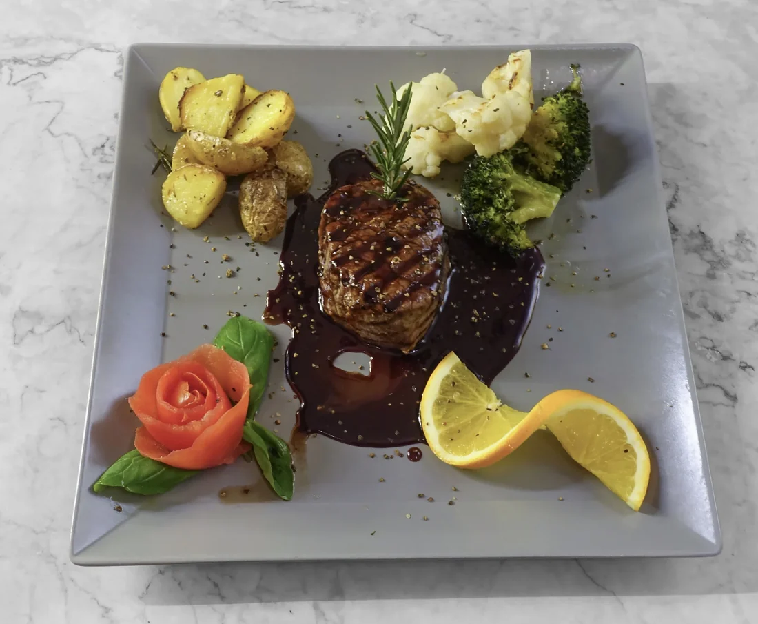 Gegrilltes Rindersteak in dunkler Sauce mit Rosmarin, Bratkartoffeln, Brokkoli, Blumenkohl, Tomatenrose und Orange