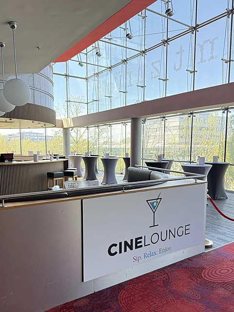 Verglaster Loungebereich mit Tresen, Stehtischen und Schild mit der Aufschrift CineLounge