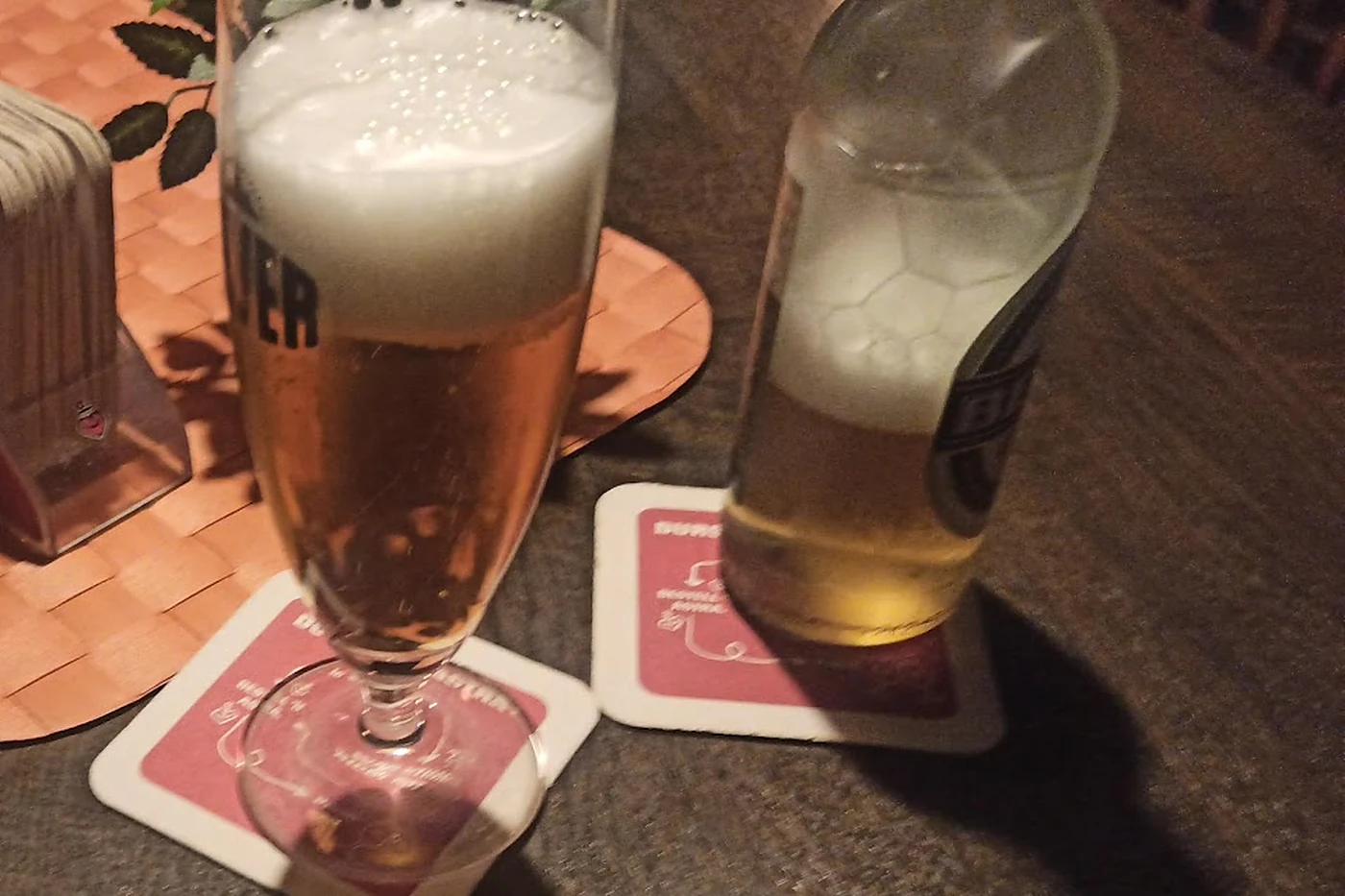 Bierglas und Flaschenbier auf Bierdeckeln, daneben ein Ständer mit Astra-Deckeln auf dem Kneipentisch