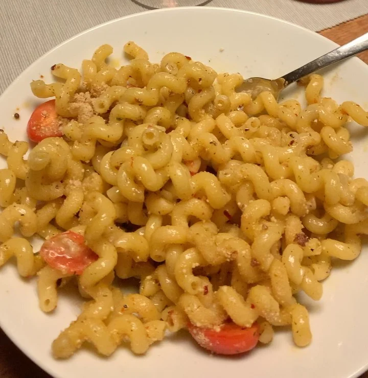 Teller mit Spiralnudeln in Öl mit Kirschtomaten, Chili und Parmesan, dahinter ein Glas Roséwein