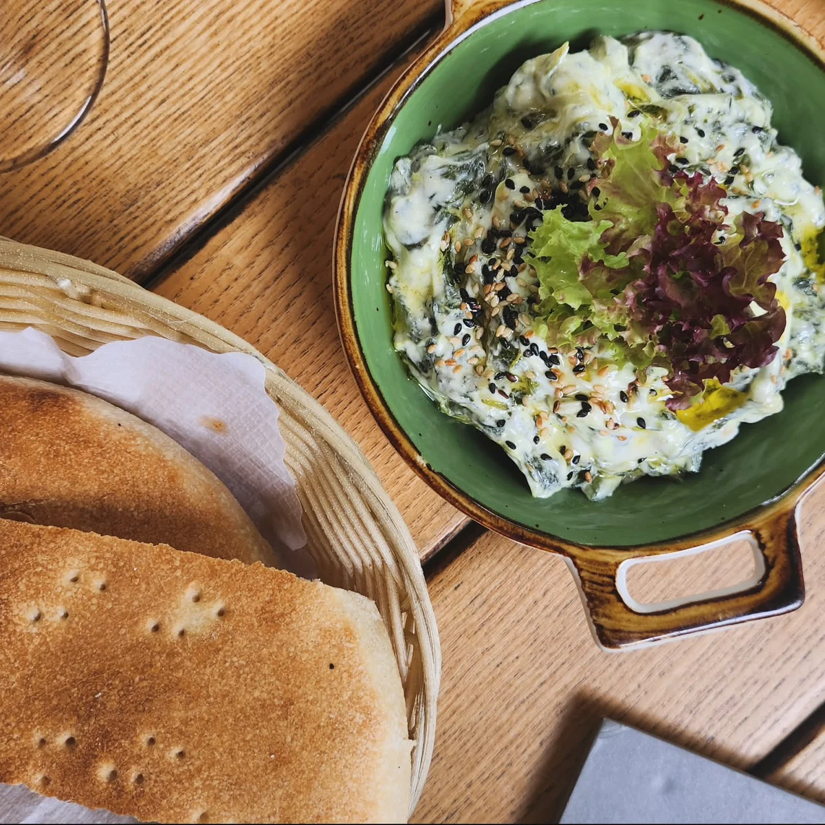 Schale mit Borani, persischem Spinat-Joghurt mit Olivenöl und schwarzem Sesam, daneben Fladenbrot im Korb