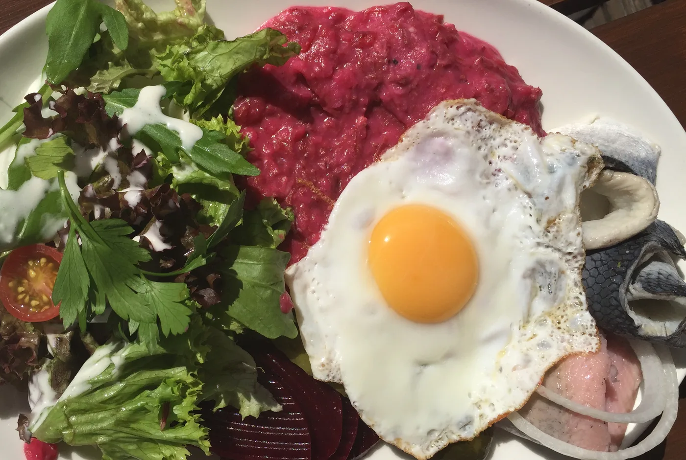 Labskaus mit Spiegelei, Roter Bete, Matjesfilet und Salat auf einem weißen Teller
