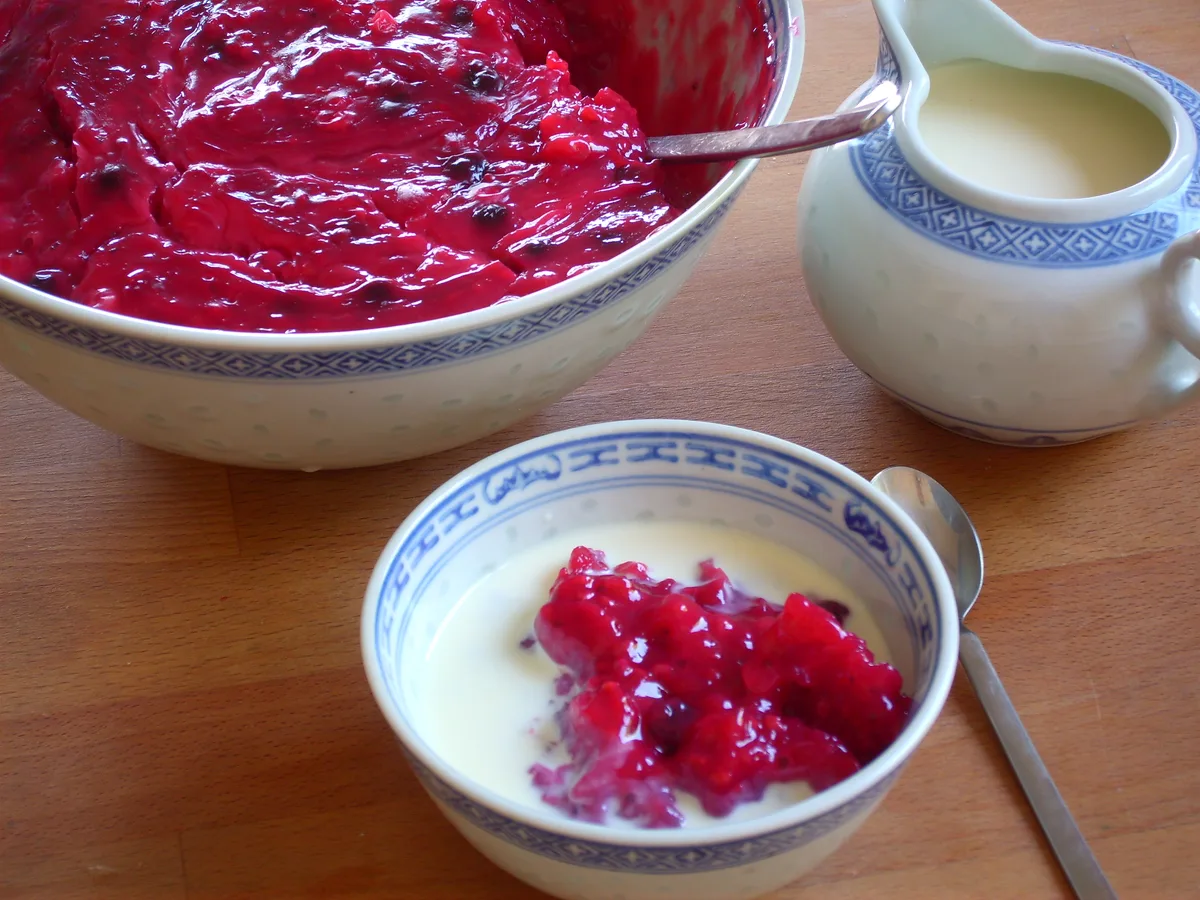 Schale Rote Grütze mit Vanillesauce, daneben eine Kanne Sauce und eine größere Schüssel