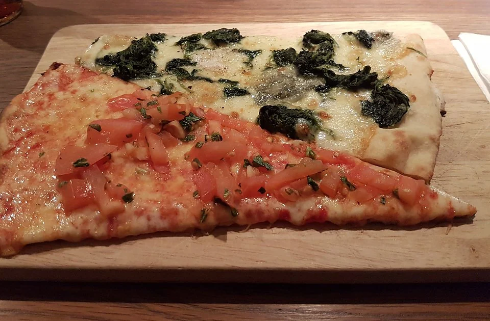 Pizzastücke mit Spinat und mit frischen Tomaten auf hellem Holzbrett
