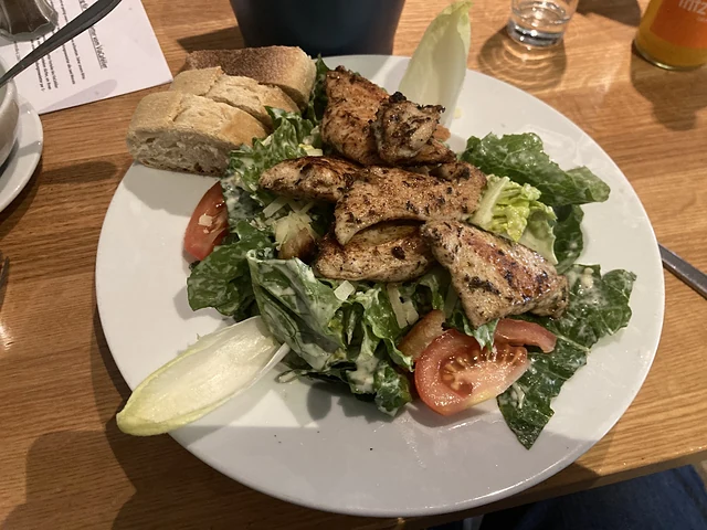 Caesar Salad mit gegrillten Hähnchenstreifen, Tomaten und Brot auf weißem Teller