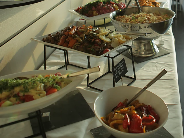 Buffet mit Salaten, gegrilltem Gemüse, Kartoffelsalat und Antipasti in Schalen und auf Platten auf einer weißen Tischdecke