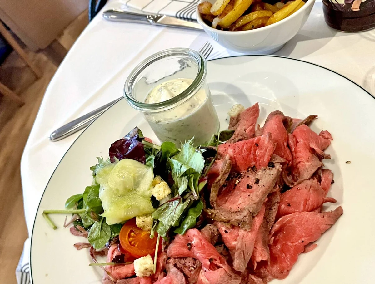 Teller mit rosa gebratenem Roastbeef, Remoulade im Glas, Salat und einer Schale Pommes