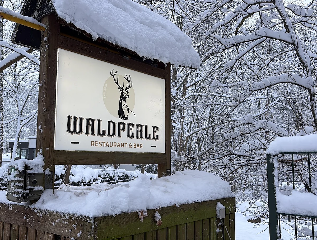 Schild mit Hirschgeweih und dem Schriftzug Waldperle Restaurant & Bar, ringsum verschneite Bäume