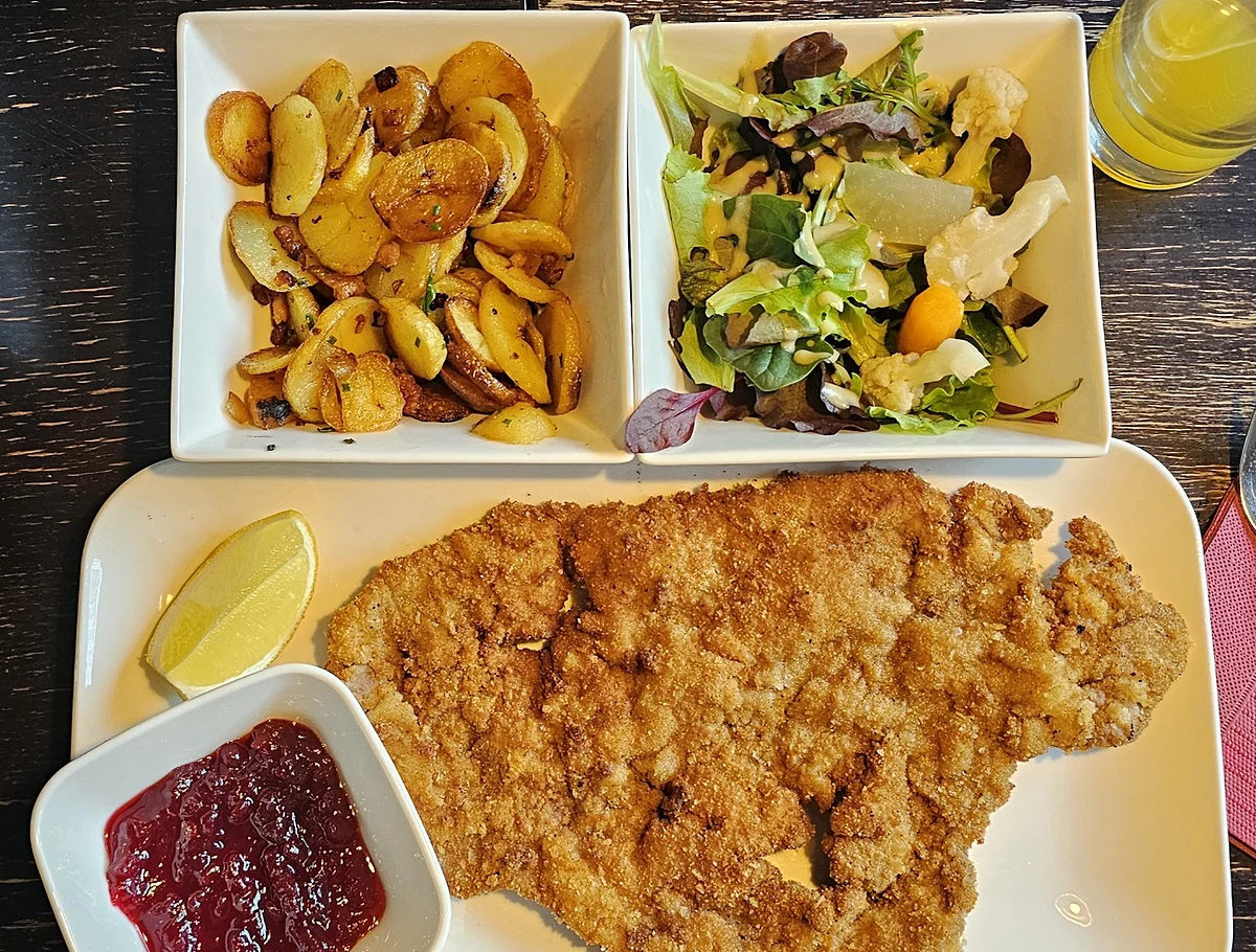 Paniertes Schnitzel mit Zitrone, Preiselbeeren, Bratkartoffeln und Salat