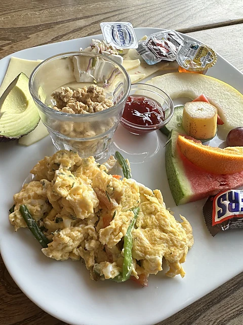 Frühstücksteller mit Rührei, Avocado, Obst, Müsli mit Joghurt und Marmelade auf einem Holztisch