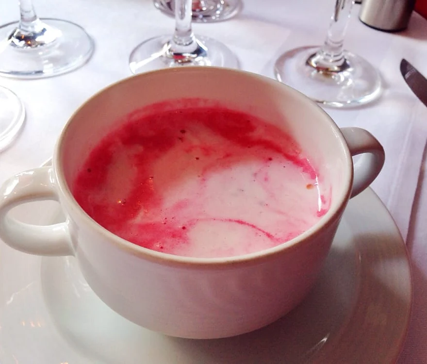 Tasse mit pinkfarbener Rote-Bete-Schaumsuppe auf weißem Tischtuch