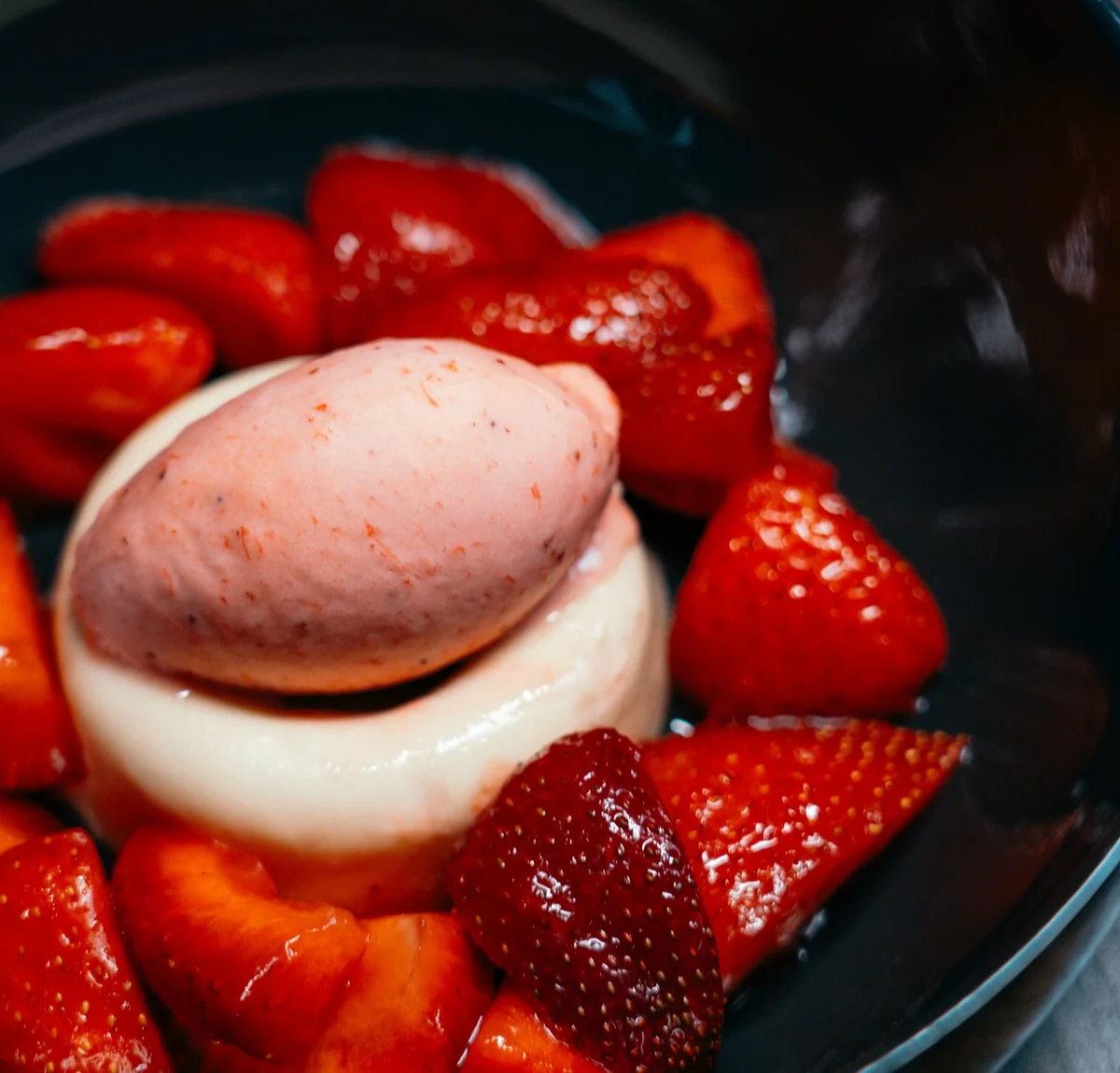 Panna cotta mit Erdbeersorbet und frischen Erdbeeren in dunkler Schale