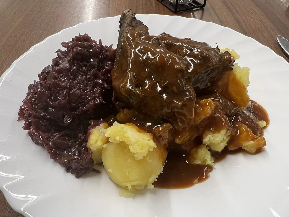 Rinderbraten mit Rotkohl, Salzkartoffeln und dunkler Sauce auf weißem Teller
